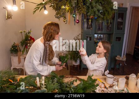 Die Tochter gibt Mutter im Innenraum der Werkstatt einen herzförmigen Zuckerstock. Die junge Frau freut sich liebevoll über das Geschenk für kleine Mädchen. Winterferien mit F Stockfoto