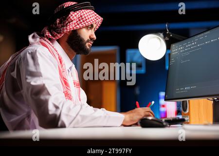 Muslimischer Mann gibt Code auf einem Desktop-PC ein. Er zeichnet sich durch seine Erfahrung in der Anwendungsprogrammierung aus und zeigt sein Know-how in der Softwareentwicklung und Algorithmen. Dieses Bild repräsentiert die sich entwickelnde Welt der digitalen Technologie. Stockfoto