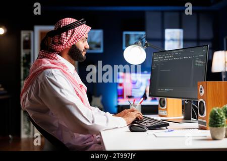 Das Bild zeigt einen arabischen Softwareentwickler, der am pc-Monitor arbeitet und an einem Verarbeitungsalgorithmus der Workstation sitzt. Muslim Coder verwendet einen Desktop-Computer, um auf der Benutzeroberfläche zu arbeiten. Stockfoto