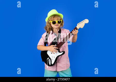 Kindermusiker spielt Gitarre wie ein Rockstar auf blauem Hintergrund im Studio. Kleiner Junge, der Gitarre spielt wie ein Rockstar Stockfoto