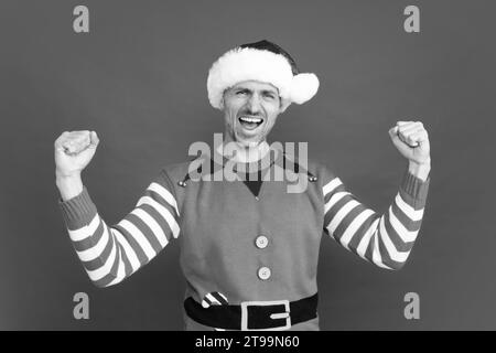 Spüren Sie den Erfolg. Fröhlicher schreiender Mann in Elfenkostüm. der weihnachtsmann mit dem weihnachtsmann-Hut Stockfoto