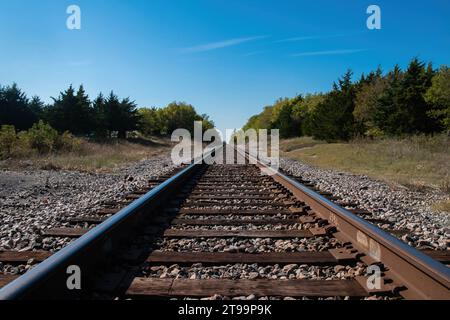 Eine Reihe von Eisenbahngleisen verschwindet am fernen Horizont, während sie an einem sonnigen Morgen über einen kleinen, von Bäumen gesäumten Hügel fahren. Stockfoto