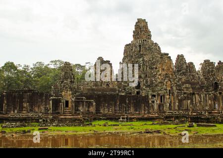 Ein Foto des Bayon Tempels vom Nordeingang. Die Schnitzereien von ruhigen Gesichtern sind auf den Sandsteintürmen zu sehen und eine sitzende Statue kann sein Stockfoto