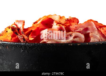 Gebratene Speckscheiben in schwarzer Pfanne isoliert auf weißem Hintergrund. Stockfoto