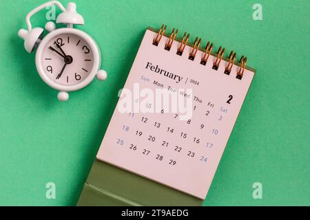 Tischkalender für Februar 2024 und Uhr auf grünem Hintergrund Stockfoto