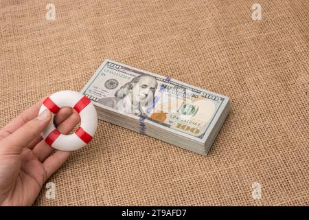 Rettungsring in der Hand über das Banknotenbündel aus US-Dollar Stockfoto