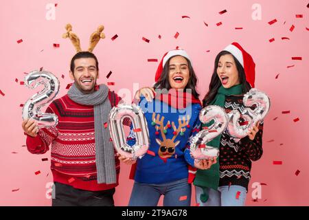 Gruppe glücklicher männlicher und weiblicher Freunde, die Pullover tragen, um Weihnachten 2023 zu feiern, im Studio Porträt in rosa Hintergrund aufgenommen Stockfoto