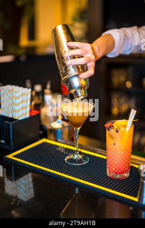 Vertikale Nahaufnahme der Hand eines Barkepers, der einen Cocktail auf ein luxuriöses Martini-Glas gießt Stockfoto