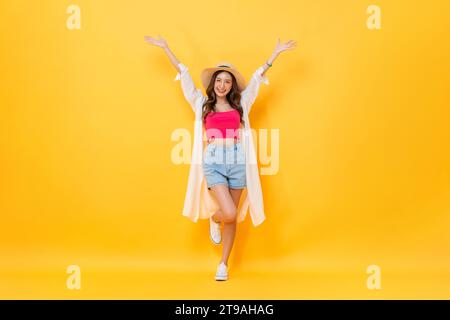 Ganzkörperporträt einer hübschen asiatischen Frau in Sommeroutfit, die lächelt und die Hände hochhebt, in farbenfroher gelber, isolierter Hintergrundaufnahme im Studio Stockfoto