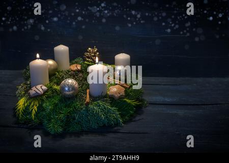 Grüner Adventskranz mit weißen Kerzen, zwei werden für den zweiten Adventskranz beleuchtet, Weihnachtsdekoration und Kekse, dunkelblauer hölzerner Hintergrund mit Stern-Bokeh, Stockfoto