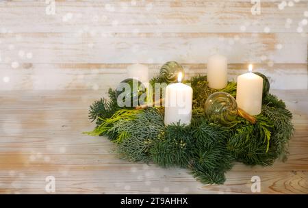 Zweiter Adventskranz, natürlicher Adventskranz mit weißen Kerzen, zwei sind beleuchtet, grüne Weihnachtskugeln aus Glas und Zimt, hölzerner Hintergrund mit sno Stockfoto