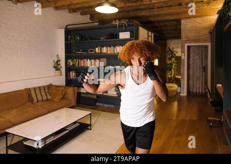 Junger afroamerikanischer Mann, der im Wohnzimmer Boxen übt. Junge Boxer, die sich zu Hause aufwärmen. Stockfoto