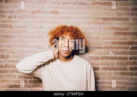 Porträt eines lächelnden jungen afroamerikanischen Mannes mit Afro-Frisur und Backsteinmauern. Stockfoto