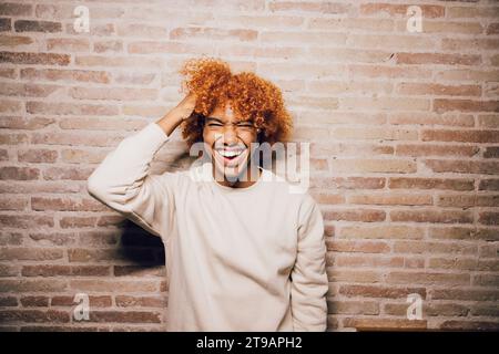 Porträt eines lächelnden jungen afroamerikanischen Mannes mit Afro-Frisur und Backsteinmauern. Stockfoto