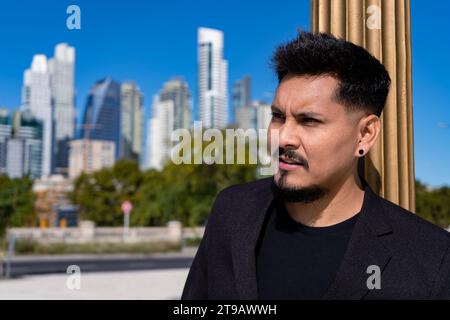 Nahaufnahme eines jungen Latino-Mannes, der sich mit ernstem Ausdruck auf eine Säule stützt. Stockfoto