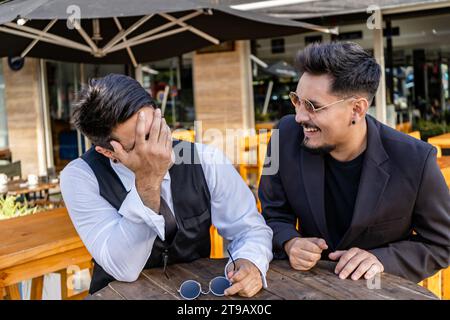 Zwei junge Latinos an einem Tisch draußen in einer Bar, die sich unterhalten und Spaß haben. Stockfoto