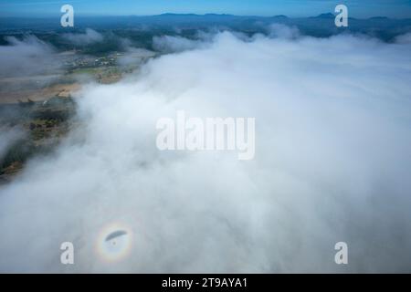 Ein Schatten eines Gleitschirms (Paramotor) mitten in einem Sonnenschein auf einer Wolke über Bergen. Stockfoto