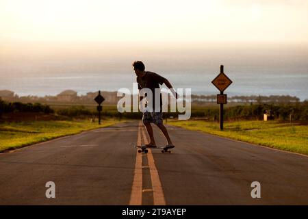 Die Perspektive eines Mannes Longboard-Skateboarden in schönem Licht einen Hügel hinunter mit dem Ozean im Hintergrund. Stockfoto