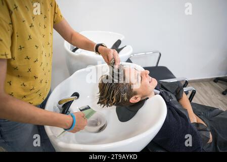 Professioneller Friseur. Waschen des Kopfes einer lächelnden Frau, nachdem sie ihr Haar geschnitten, gefärbt und Highlights hinzugefügt hat. Stockfoto