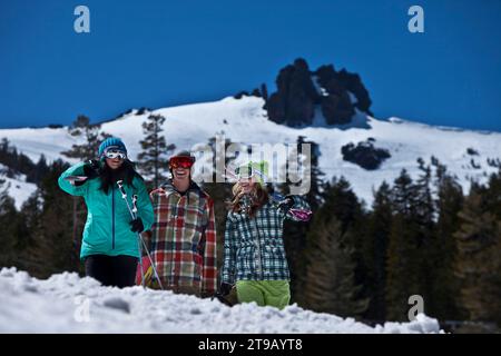 Drei Freunde (ein Mann und zwei Frauen) hängen mit Skiern und einem Snowboard vor einem Skigebiet ab. Stockfoto