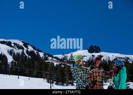 Drei Freunde (ein Mann und zwei Frauen) hängen mit Skiern und einem Snowboard vor einem Skigebiet ab. Stockfoto