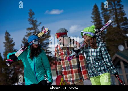 Drei Freunde (ein Mann und zwei Frauen) hängen mit Skiern und einem Snowboard vor einem Skigebiet ab. Stockfoto