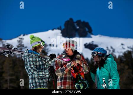 Drei Freunde (ein Mann und zwei Frauen) hängen mit Skiern und einem Snowboard vor einem Skigebiet ab. Stockfoto