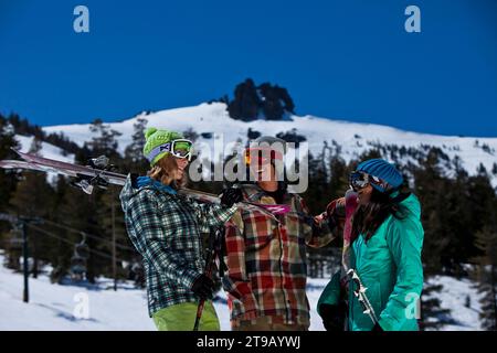 Drei Freunde (ein Mann und zwei Frauen) hängen mit Skiern und einem Snowboard vor einem Skigebiet ab. Stockfoto