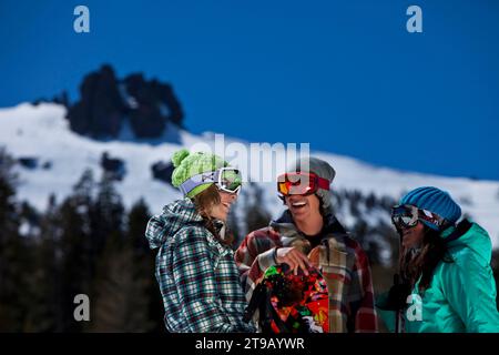 Drei Freunde (ein Mann und zwei Frauen) hängen mit Skiern und einem Snowboard vor einem Skigebiet ab. Stockfoto