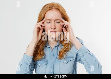 Gestresstes Frauenporträt mit rotem Haar, das Migräne-Kopfschmerzen hat, den Kopf vor Schmerzen und Stress isoliert über weißem Hintergrund hält Stockfoto