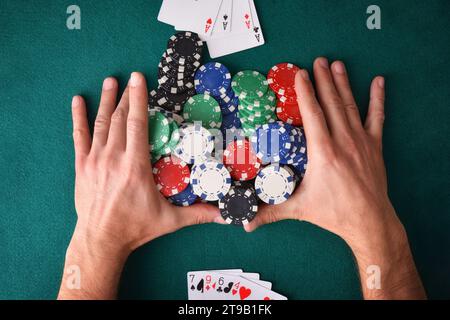 Gewinnhand mit Poker aus Assen und einem Haufen Chips auf dem Tisch an einem Ende und Verlierer ohne Spiel vorne auf grüner Matte. Draufsicht. Stockfoto