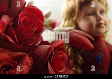 Rote künstliche Rosen mit einem unscharfen Puppengesicht im Hintergrund Stockfoto