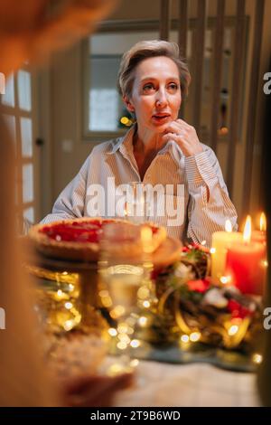 Vertikales Porträt einer glücklichen kaukasischen Frau mittleren Alters, die sich zu Hause mit der Familie trifft, um Weihnachten zu feiern. Freunde versammelten sich um Tisch Stockfoto