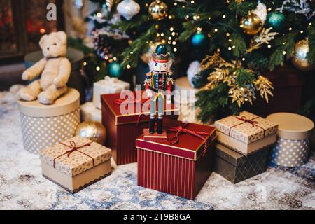 Nussknacker-Soldat wacht zwischen eingewickelten Weihnachtsgeschenken und einem Teddybären mit einem Weihnachtsbaum im Hintergrund Stockfoto