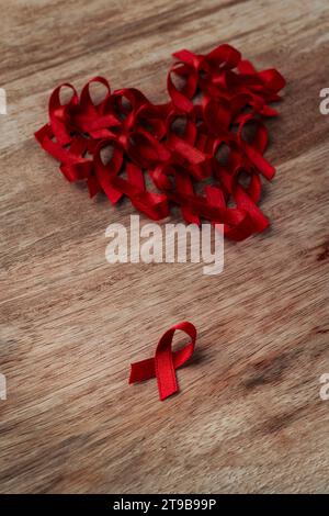 Nahaufnahme einiger roter Bewusstseinsbänder, für den Kampf gegen AIDS, angeordnet als Herz auf einer hölzernen Oberfläche Stockfoto