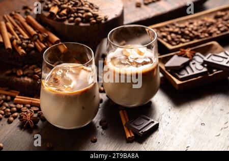 Irischer Kaffee- und Cremecocktail in Gläsern mit Eis auf einem alten Holzhintergrund. Kaffeebohnen, Zimt, Anise und Schokoladenstücke sind verstreut Stockfoto