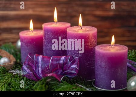 Augsburg, Bayern, Deutschland - 24. November 2023: Weihnachtskranz mit vier brennenden lila Kerzen zur Adventszeit *** Weihnachtskranz mit vier brennenden lila Kerzen zur Adventszeit Stockfoto