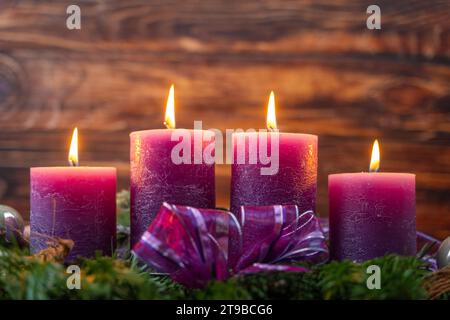 Augsburg, Bayern, Deutschland - 24. November 2023: Weihnachtskranz mit vier brennenden lila Kerzen zur Adventszeit *** Weihnachtskranz mit vier brennenden lila Kerzen zur Adventszeit Stockfoto