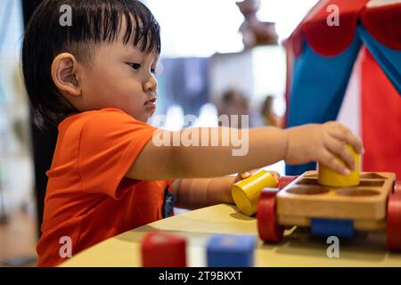 Kleinkinder spielen zu Hause mit einem Holzspielzeug. Kleinkinder spielen mit einem farbigen Lernspielzeug. Kindliche Entwicklung. Stockfoto