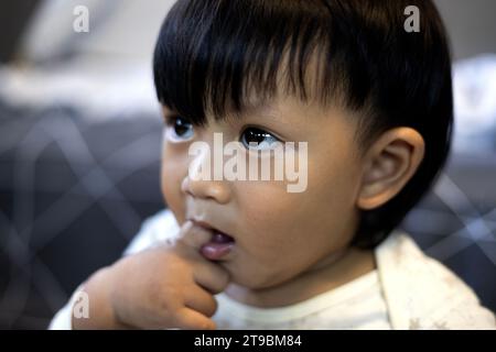 Schließen Sie den asiatischen Jungen, der Finger in den Mund lutscht. Entzückender kleiner asiatischer Junge, der Finger im Mund lutscht. Stockfoto