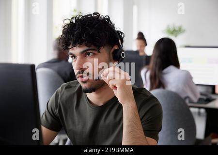 Mann, der im Büro ein Headset mit einem Desktop-PC trägt Stockfoto