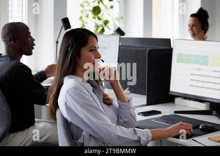 Frau, die im Büro ein Headset mit einem Desktop-PC trägt Stockfoto