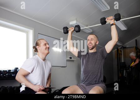 Mann, der mit Hantel trainiert, mit Trainer, der seinen Fortschritt überprüft Stockfoto