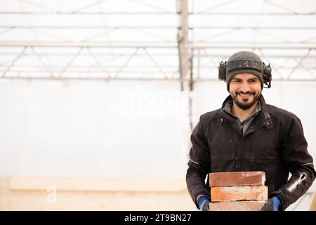 Porträt eines glücklichen Bauarbeiters, der Ziegelsteine trägt Stockfoto