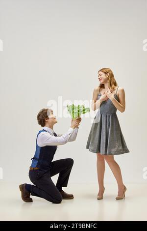 Es ist kein Geschenk, aber der Gedanke zählt. Hübsche Frau, sehr glücklich mit einem Salatstrauß von ihrem geliebten Kerl, der vor ihr auf einem Knie liegt Stockfoto