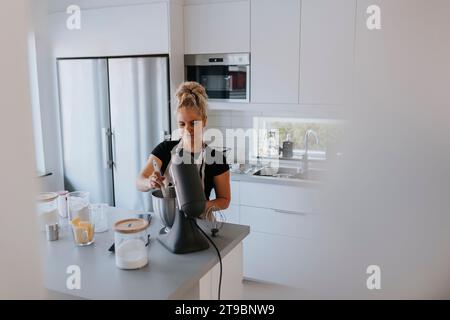 Junge Frau, die Standmixer in der Küche benutzt Stockfoto