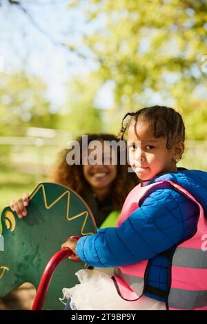 Mädchen, das auf dem Spielplatz sitzt und in die Kamera schaut Stockfoto