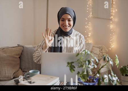 Glückliche Freelancerin, die bei Videogesprächen über Laptop zuhause zuwinkt Stockfoto