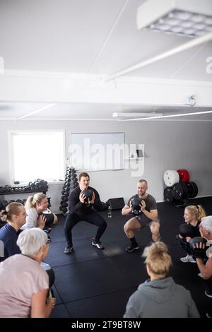 Gruppenübungen mit Kettlebells während des Hockens im Fitnessstudio Stockfoto
