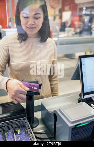 Lächelnde junge Frau, die am Kassenschalter im Supermarkt per Smartphone bezahlt Stockfoto